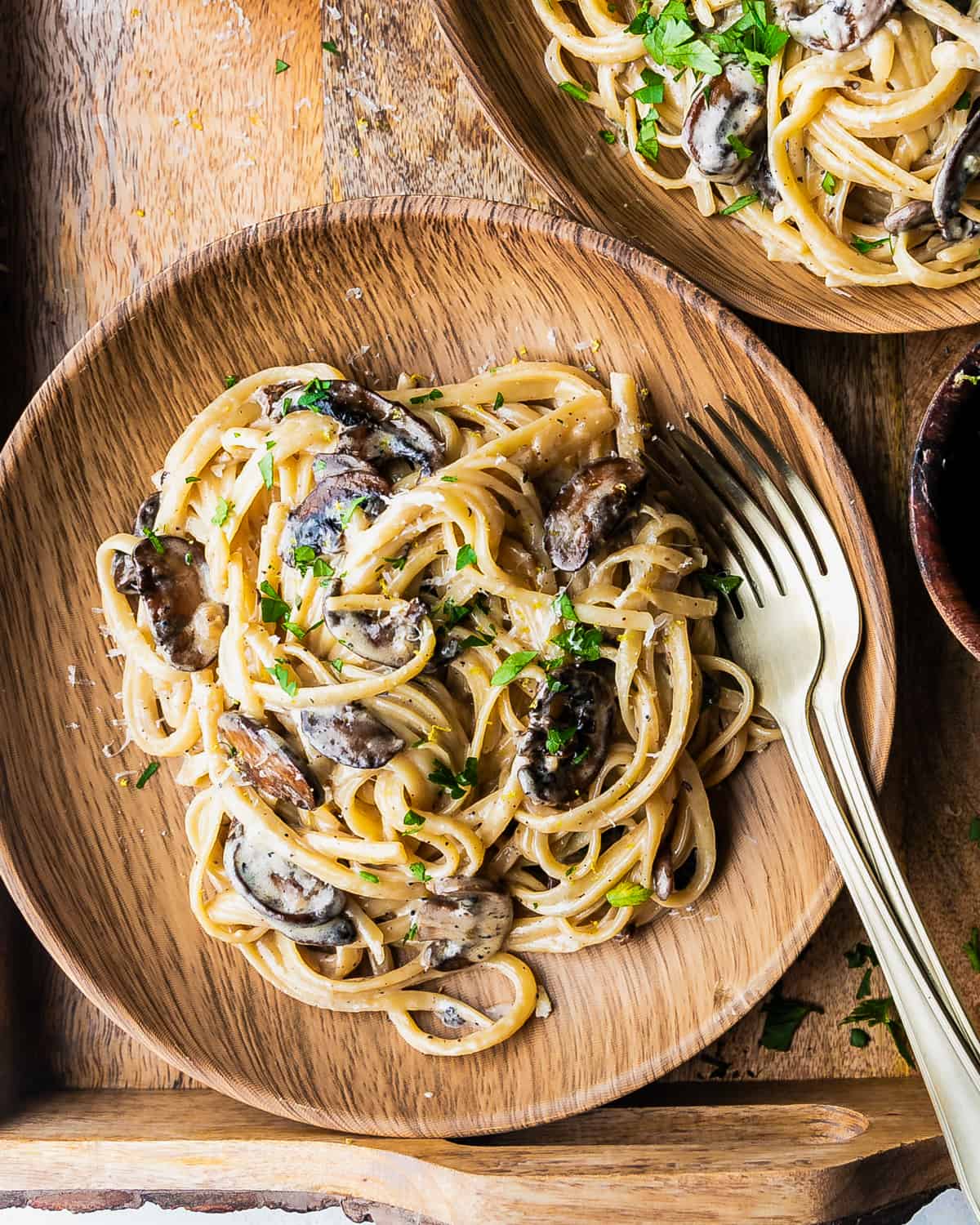 Creamy truffle mushroom fettuccine topped with parmesan, lemon zest and parsley in a wooden bowl